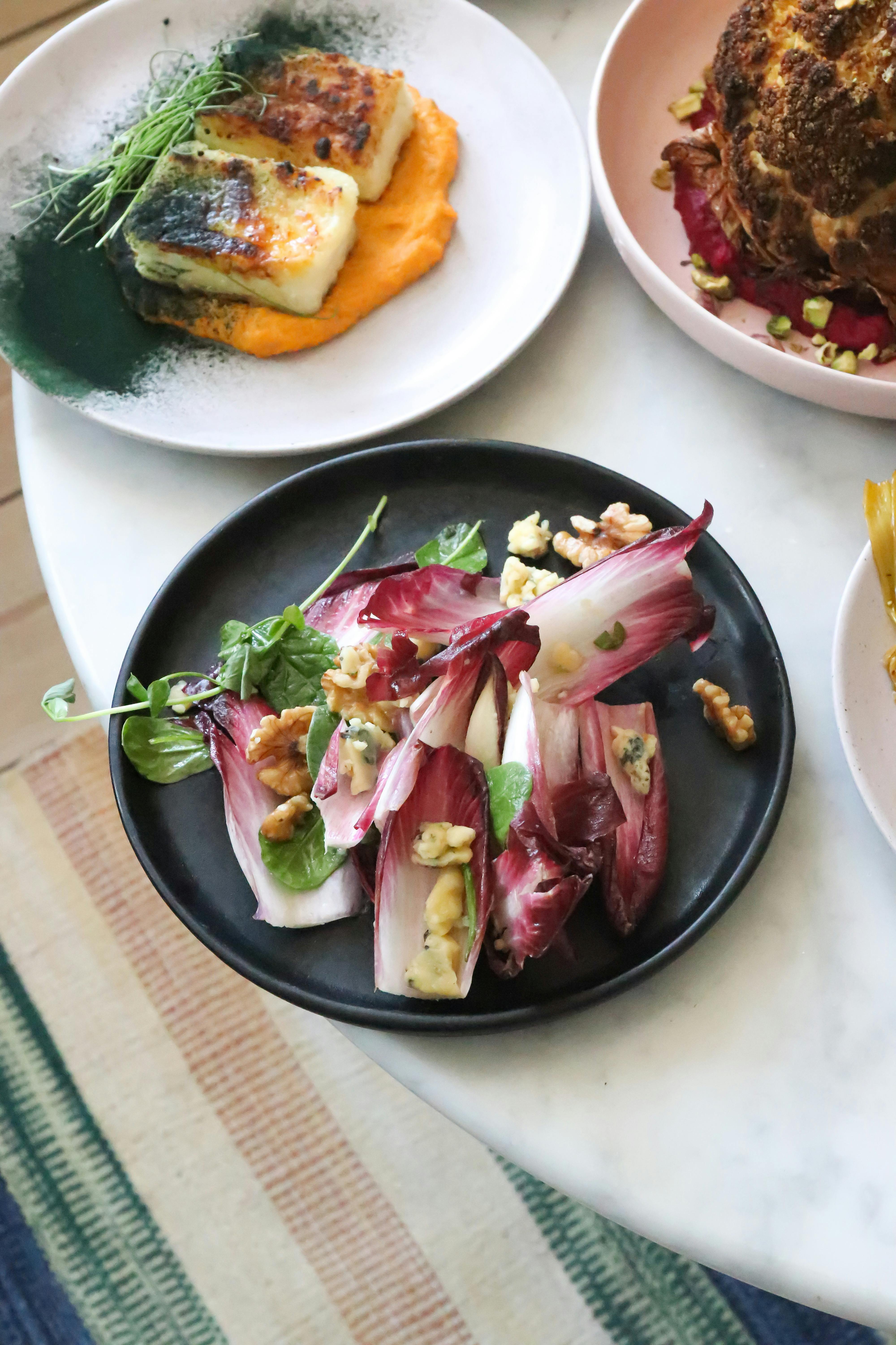Svart tallrik med en sallad av rosésallad, grönsaker och valnötter.